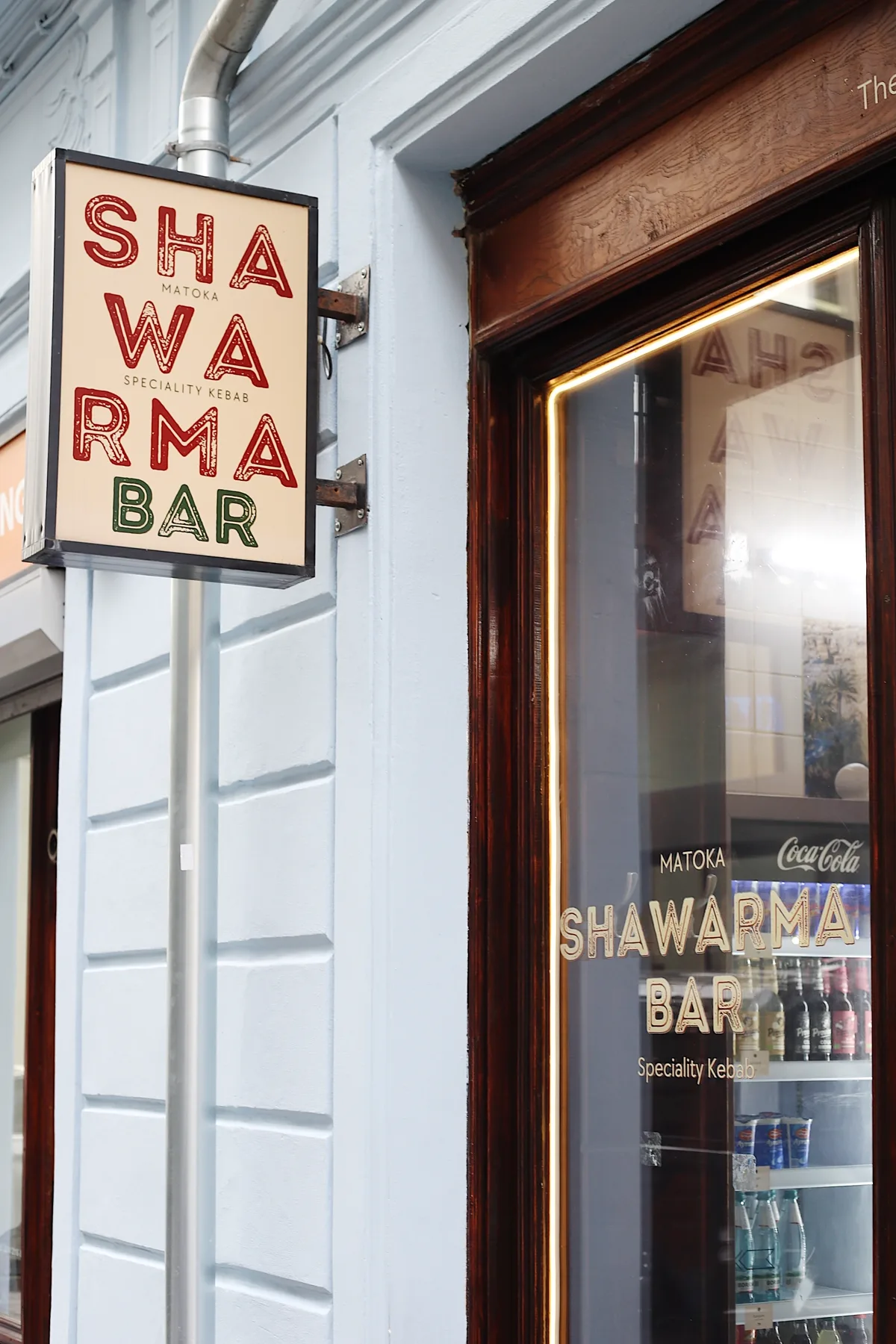 Ručně psaný nápis MATOKA Shawarma Bar vedle výlohy restaurace.